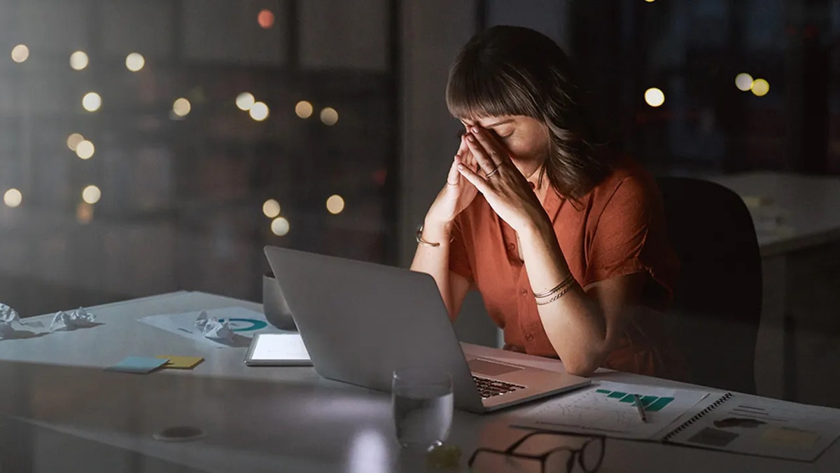 businesswoman looking stressed out while working on a laptop in an office at night