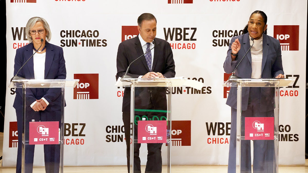 Three Democratic candidates stand on a debate stage at a university auditorium before an audience.