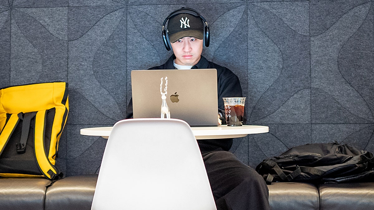 A man works on a laptop in a cafe with an iced coffee.