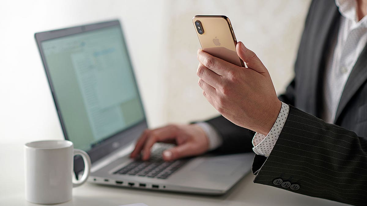 Man holding phone while typing on computer.