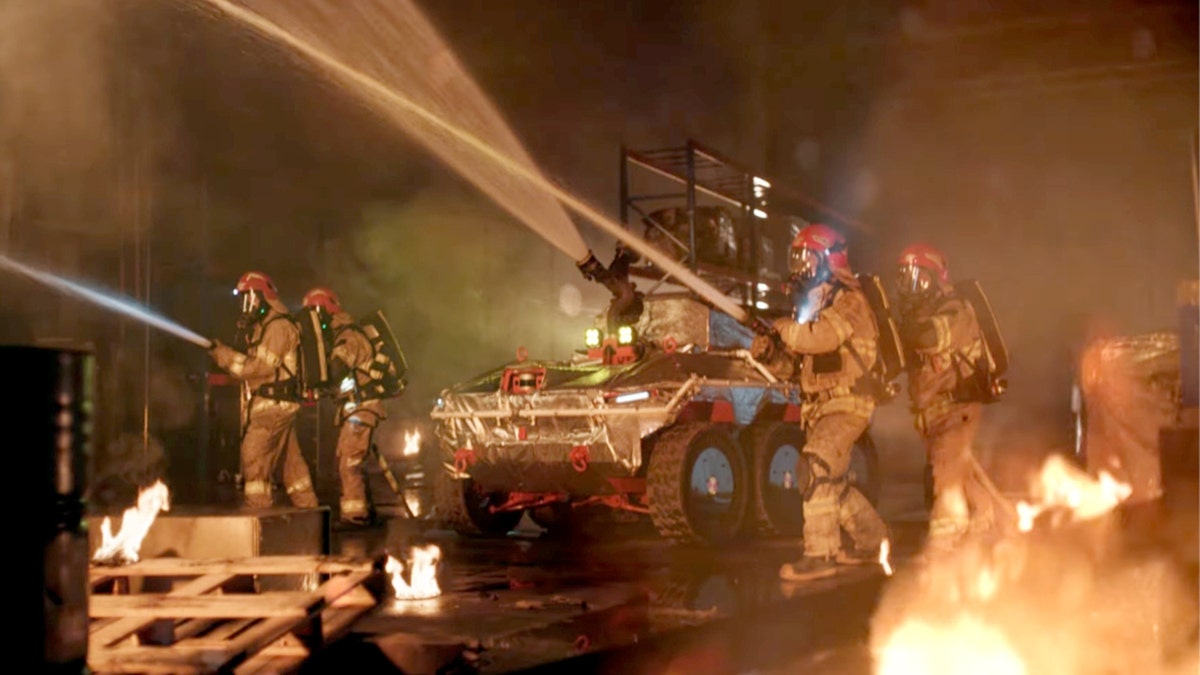 Firefighters work with the Hyundai robot, spraying water.