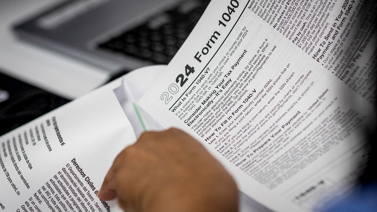 A person flips through tax forms, including the 2024 Form 1040.