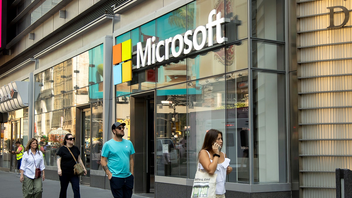 People walk in front of an office building with a Microsoft sign.