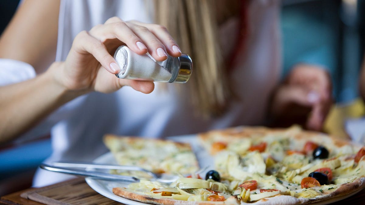 Woman salting a pizza in a kitchen
