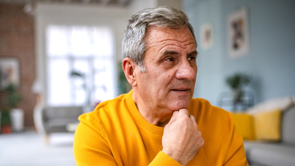 Worried older man sitting indoors with hands clasped