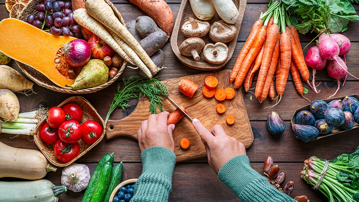 Woman chopping carrots on a table with autumnal fruits and vegetables