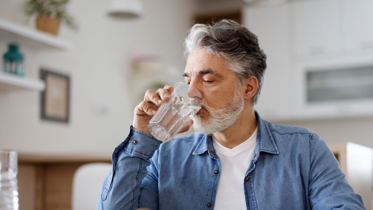 A man drinking water from a clear glass.