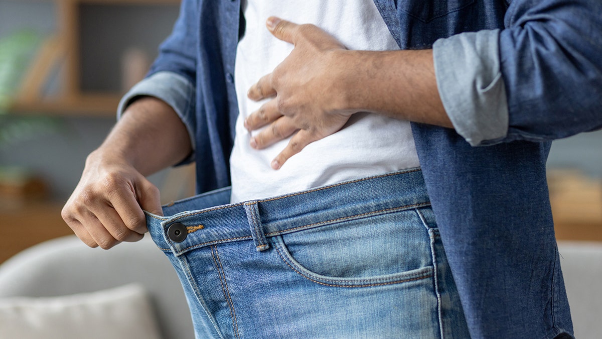 A man holding out the waist of his oversized jeans to show weight loss.