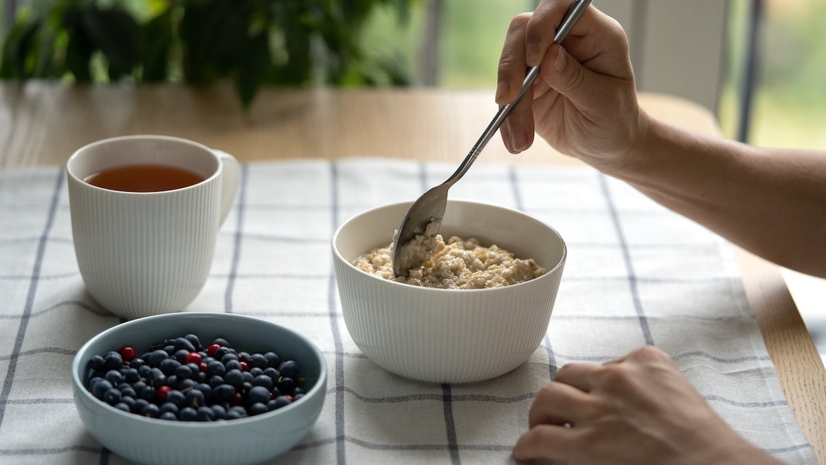 Woman eating oatmeal porridge with summer berries at a table