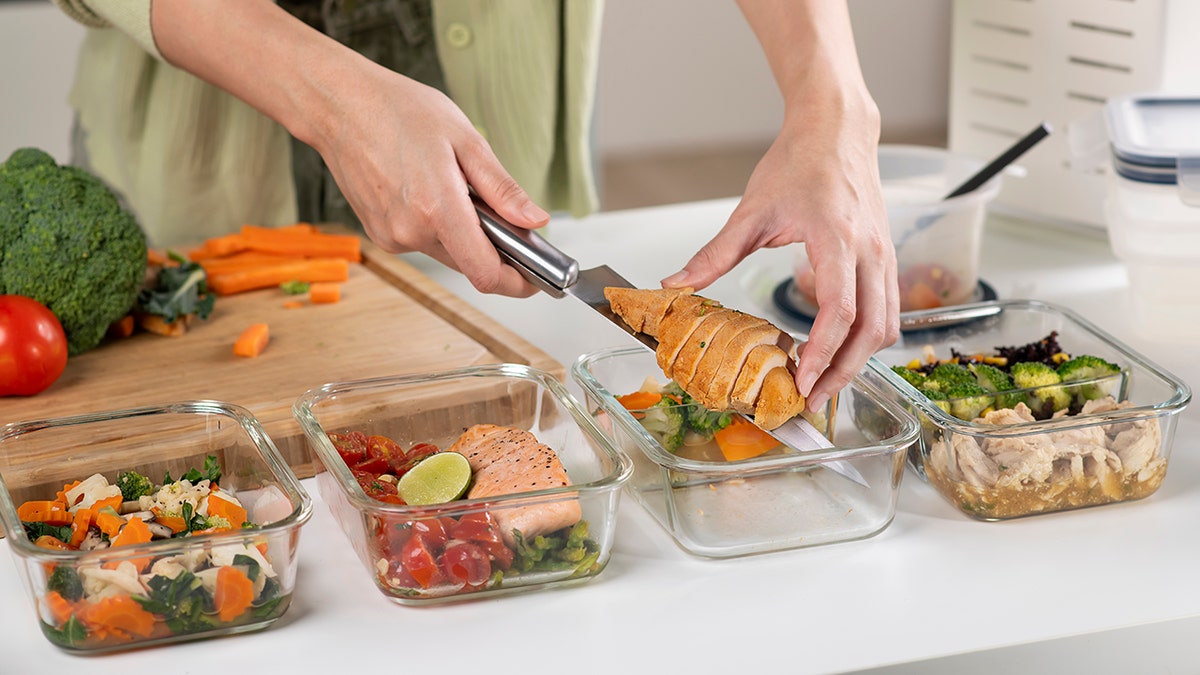 Woman preparing healthy homemade meal with chicken, vegetables, and salmon at home