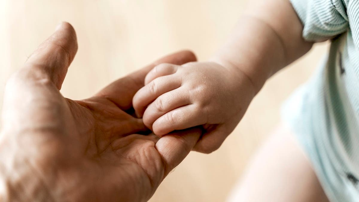 Father holding newborn baby's hand with tenderness