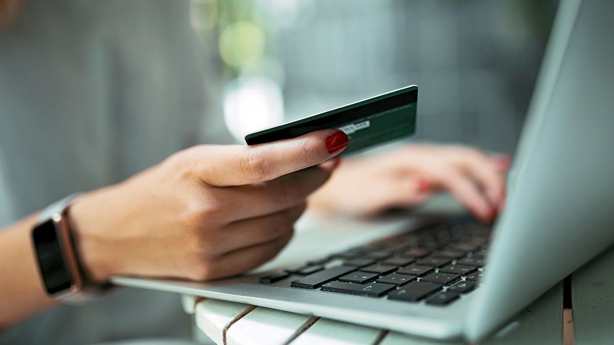 A woman holding a credit card next to an open laptop.